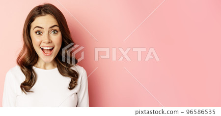 Close up of enthusiastic brunette girl with makeup, smiling and looking happy at camera, posing against pink background Close up of enthusiastic brunette girl with makeup, smiling and looking happy at camera, posing against pink background 96586535