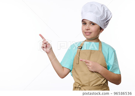 Adorable teenage boy dressed as a chef pastry or baker confectioner, wearing a white hat and beige apron, looks at camera and points at free space for promotional text, isolated over white background Adorable teenage boy dressed as a chef pastry or baker confectioner, wearing a white hat and beige apron, looks at camera and points at free space for promotional text, isolated over white background 96586536