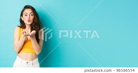 Beautiful glamour girl in summer clothes pucker her lips, blowing air kiss, sending mwah in palms, standing over blue background Beautiful glamour girl in summer clothes pucker her lips, blowing air kiss, sending mwah in palms, standing over blue background 96586554