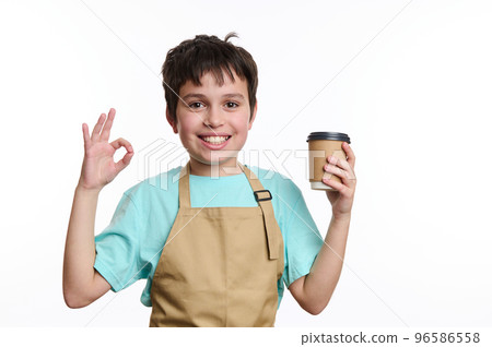 Amazing teenage boy - little barista bartender in chef apron, showing OK sign while selling hot takeaway drink in paper mug, smiling looking at camera, isolated on white background with free ad space Amazing teenage boy - little barista bartender in chef apron, showing OK sign while selling hot takeaway drink in paper mug, smiling looking at camera, isolated on white background with free ad space 96586558