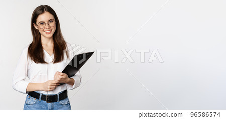 Portrait of corporate woman holding clipboard at work, standing in formal outfit over white background Portrait of corporate woman holding clipboard at work, standing in formal outfit over white background 96586574