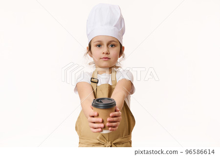 Isolated portrait on white background of cute baby girl wearing a white chef's hat and beige apron, holding, selling a hot drink in a paper cup to go, looking at camera, isolated over white background Isolated portrait on white background of cute baby girl wearing a white chef's hat and beige apron, holding, selling a hot drink in a paper cup to go, looking at camera, isolated over white background 96586614