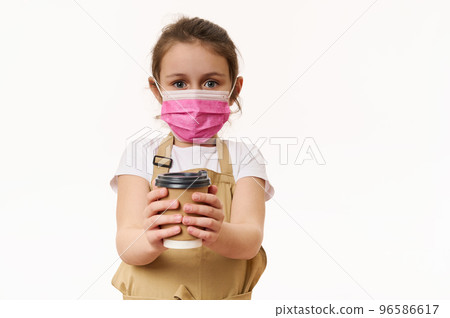 Caucasian little child girl wearing safety medical mask, dressed as barista, bartender with a hot drink in paper cup, isolated on white background. Cafe restaurant on pandemic lockdown. Takeaway food. Caucasian little child girl wearing safety medical mask, dressed as barista, bartender with a hot drink in paper cup, isolated on white background. Cafe restaurant on pandemic lockdown. Takeaway food. 96586617
