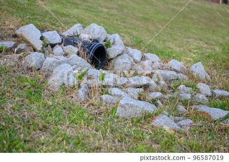plastic storm water outlet with rip-rap protruding from a grass embankment  96587019