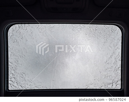 Inside a vehicle looking up to a sunroof with water droplets  96587024