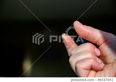 Caucasian hand compressing a metal spring between a thumb and finger Caucasian hand compressing a metal spring between a thumb and finger 96587041