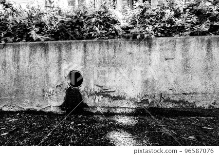 Stormwater drain outlet in an urban area with seepage discoloring a concrete barrier  96587076