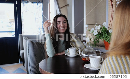 Young brunette girl smiling while sitting in a cafe. A young woman in a cafe calls the waiter. Positive emotions, laughter. Girl with a blanket in a cafe Young brunette girl smiling while sitting in a cafe. A young woman in a cafe calls the waiter. Positive emotions, laughter. Girl with a blanket in a cafe 96587193