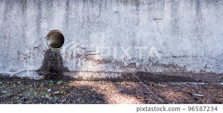Stormwater drain outlet in an urban area with seepage discoloring a concrete barrier  96587234