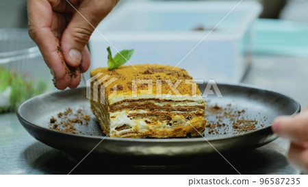A piece of cake on a plate. The chef sprinkles the cake with chocolate chips. Sweet piece of cake. Delicious honey cake on a plate A piece of cake on a plate. The chef sprinkles the cake with chocolate chips. Sweet piece of cake. Delicious honey cake on a plate 96587235
