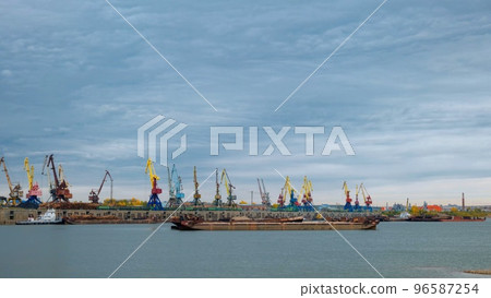 River port. Port cranes on the bank of the river. Embankment of the river port, a barge at the quay wall. Large port cranes on the river. Extraction and transportation of sand 96587254