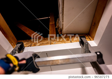 hand gripping the last rung on a ladder leading to an open attic 96587273