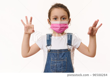 Adorable Caucasian little girl wearing pink protective medical mask, gestures with hands, shows OK signs, looks at camera, isolated over white background. Free space. Pediatrics. Health care. Medicine Adorable Caucasian little girl wearing pink protective medical mask, gestures with hands, shows OK signs, looks at camera, isolated over white background. Free space. Pediatrics. Health care. Medicine 96588264