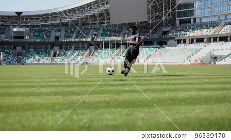 African American man playing football on the stadium field. A man runs with a soccer ball across the field. African American man playing football on the stadium field. A man runs with a soccer ball across the field. 96589470
