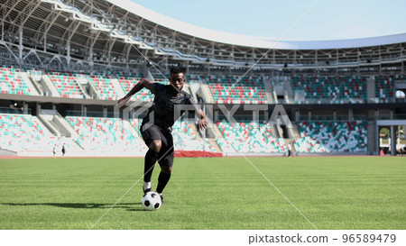 African American man playing football on the stadium field. A man runs with a soccer ball across the field. African American man playing football on the stadium field. A man runs with a soccer ball across the field. 96589479