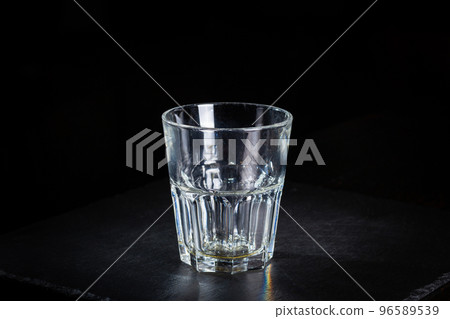 Faceted empty glass stands on a black slate plate. Faceted empty glass stands on a black slate plate. 96589539