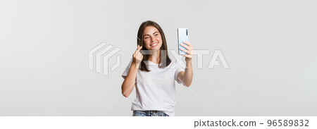 Happy beautiful young woman showing heart gesture and taking selfie on smartphone and smiling 96589832