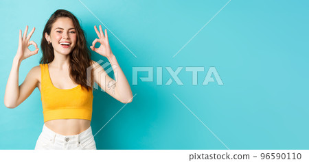Young carefree woman say yes and nod in approval, showing okay gestures to praise good choice, show perfect body in summer outfit, ready for vacation, standing over blue background Young carefree woman say yes and nod in approval, showing okay gestures to praise good choice, show perfect body in summer outfit, ready for vacation, standing over blue background 96590110