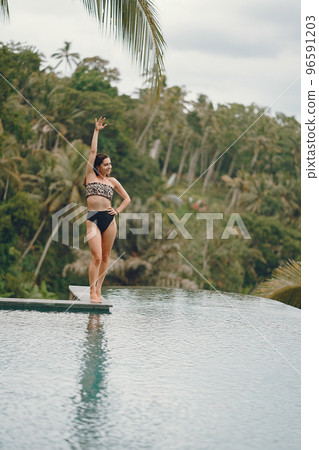 Woman sititng by the swimming pool. Lady in a swimsuit. Girl relaxing by the pool at a beach club in Bali Indonesia 96591203