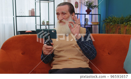 Grandfather man taking selfie on smartphone communicating video call home online with subscribers Grandfather man taking selfie on smartphone communicating video call home online with subscribers 96591657