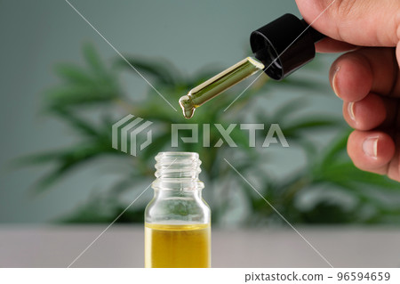 Legalized cannabis sativa hemp leaf and container of CBD oil with dropper lid. 96594659