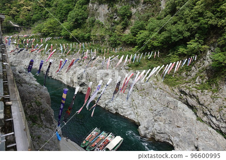 A lot of carp streamers and a clear river flowing under the cliffs and a sightseeing boat A lot of carp streamers and a clear river flowing under the cliffs and a sightseeing boat 96600995