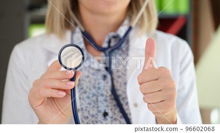 Woman practitioner posing in clinic office showing stethoscope and thumb up gesture Woman practitioner posing in clinic office showing stethoscope and thumb up gesture 96602068
