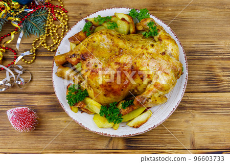 Baked whole chicken with potato and Christmas decorations on a wooden table. Top view Baked whole chicken with potato and Christmas decorations on a wooden table. Top view 96603733