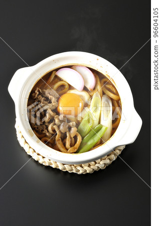 A bird's-eye view of hot miso stewed udon with beef, shimeji mushrooms, green onions, kamaboko, and egg yolk on a black background 96604105