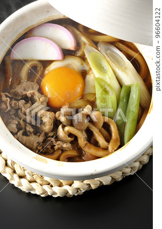 A bird's-eye view of hot miso stewed udon with beef, shimeji mushrooms, green onions, kamaboko, and egg yolk on a black background 96604122