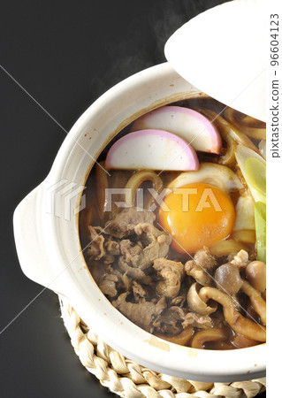 A bird's-eye view of hot miso stewed udon with beef, shimeji mushrooms, green onions, kamaboko, and egg yolk on a black background 96604123