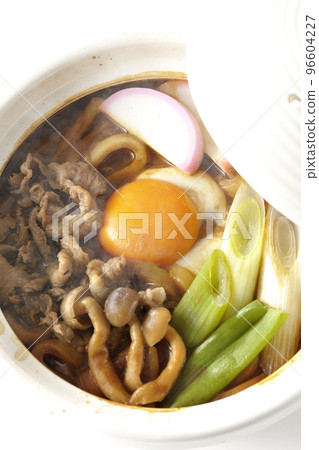 Overhead view of hot miso stewed udon with beef, shimeji mushrooms, long onion, kamaboko, and egg yolk on a white background Overhead view of hot miso stewed udon with beef, shimeji mushrooms, long onion, kamaboko, and egg yolk on a white background 96604227