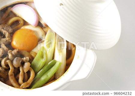 Overhead view of hot miso stewed udon with beef, shimeji mushrooms, long onion, kamaboko, and egg yolk on a white background Overhead view of hot miso stewed udon with beef, shimeji mushrooms, long onion, kamaboko, and egg yolk on a white background 96604232