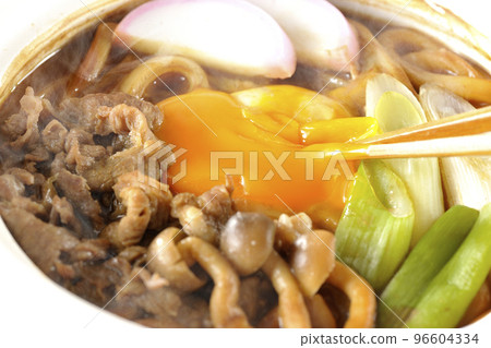 Chop the yolk of piping hot miso stewed udon with beef, shimeji mushrooms, green onion, kamaboko, and egg yolk with chopsticks. 96604334