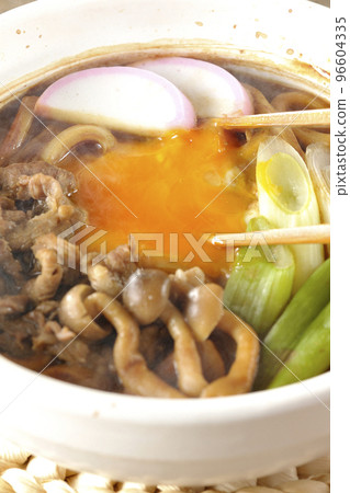 Chop the yolk of piping hot miso stewed udon with beef, shimeji mushrooms, green onion, kamaboko, and egg yolk with chopsticks. 96604335
