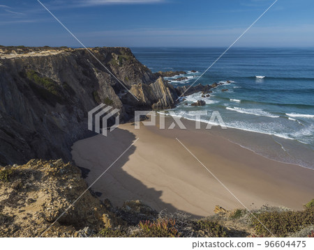 View of empty Praia da Amalia beach with ocean waves, cliffs and stones, wet golden sand and green vegetation at wild Rota Vicentina coast, Odemira, Portugal. View of empty Praia da Amalia beach with ocean waves, cliffs and stones, wet golden sand and green vegetation at wild Rota Vicentina coast, Odemira, Portugal. 96604475