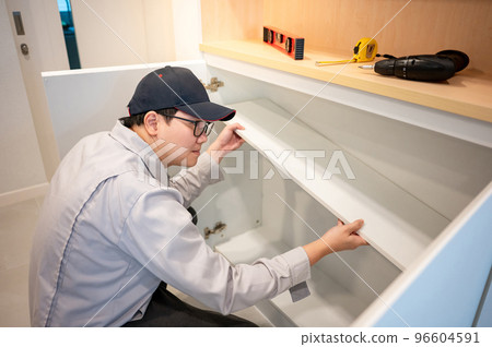 Asian male furniture assembler installing cabinet panel 96604591
