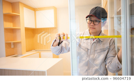 Asian male furniture assembler using tape measure on cabinet Asian male furniture assembler using tape measure on cabinet 96604719