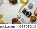 Flat lay festive composition with photo camera and colorful Christmas decorations on white wooden background with space for text 96605219
