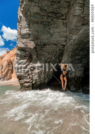 Woman swimsuit sea. Attractive blonde woman in a black swimsuit enjoying the sea air on the seashore around the rocks. Travel and vacation concept. 96605984