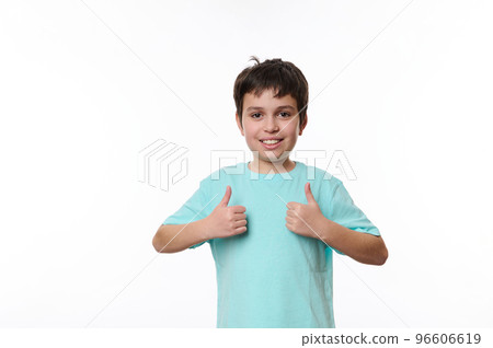 Portrait of Caucasian handsome pleasant teenage child boy in blue casual t-shirt, smiling pleasantly, looking at camera, showing thumbs up, isolated on white background with space for promotional text 96606619