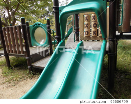 A children's playground with a green slide, located in the park's plaza. 96606799