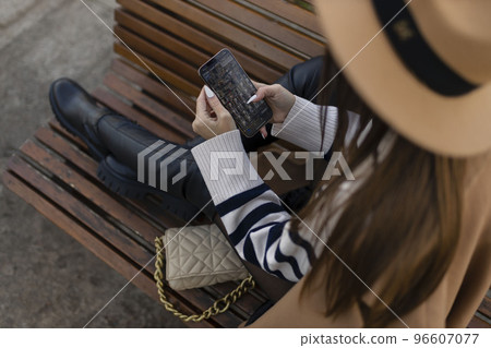 Attractive cheerful brunette girl in trench coat with coffee to go happily using cellphone outdoor Attractive cheerful brunette girl in trench coat with coffee to go happily using cellphone outdoor 96607077