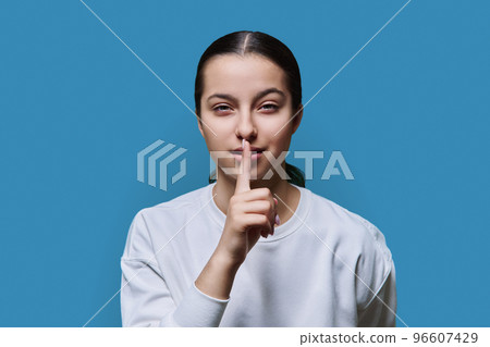 Teen girl showing silent gesture with finger on lips, blue background 96607429