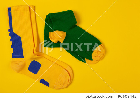A pair of green socks and a pair of yellow socks, lie side by side on a yellow background 96608442