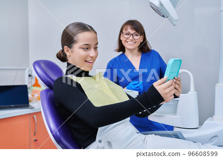 Happy female with mirror sitting in dentist chair looking at healthy teeth 96608599