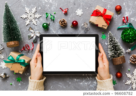 Christmas online shopping from home, female hands holding tablet pc with blank white display top view. woman hand holding tablet with blank screen, Christmas tree and gifts on background Christmas online shopping from home, female hands holding tablet pc with blank white display top view. woman hand holding tablet with blank screen, Christmas tree and gifts on background 96608782