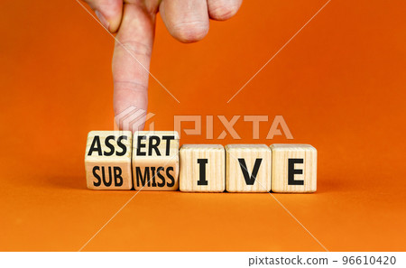 Submissive or assertive symbol. Concept words Submissive and assertive on wooden cubes. Businessman hand. Beautiful orange background. Business, psychological submissive assertive concept. Copy space. Submissive or assertive symbol. Concept words Submissive and assertive on wooden cubes. Businessman hand. Beautiful orange background. Business, psychological submissive assertive concept. Copy space. 96610420