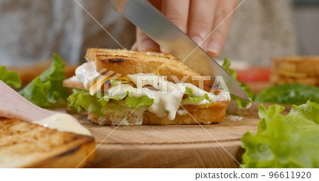 A chef cuts a sandwich in half with a sharp knife on a wooden board in the kitchen A chef cuts a sandwich in half with a sharp knife on a wooden board in the kitchen 96611920