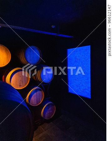 Old cellar with illuminated stacked oak barrels and bottles in a winery 96612147